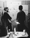A black and white photo of two individuals engrossed in discussion in front of a wall filled with various sticky notes and papers, illuminated by a desk lamp, indicative of an in-depth user experience session A black and white photo of two individuals engrossed in discussion in front of a wall filled with various sticky notes and papers, illuminated by a desk lamp, indicative of an in-depth user experience session